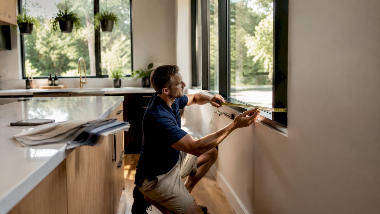 Man measuring shutter blinds inside window recess