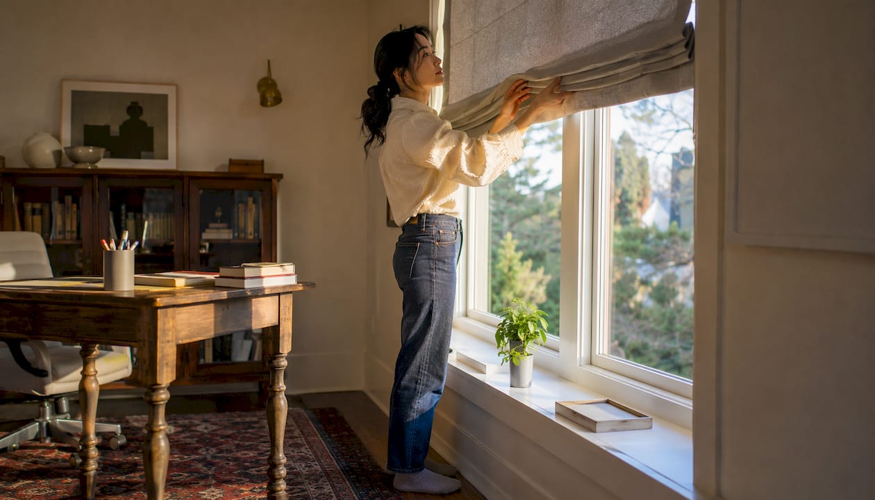 Woman adjusting wooden blinds in living room