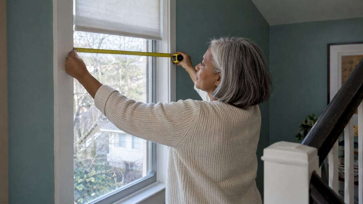 Homeowner measures a tall stair window for custom shades