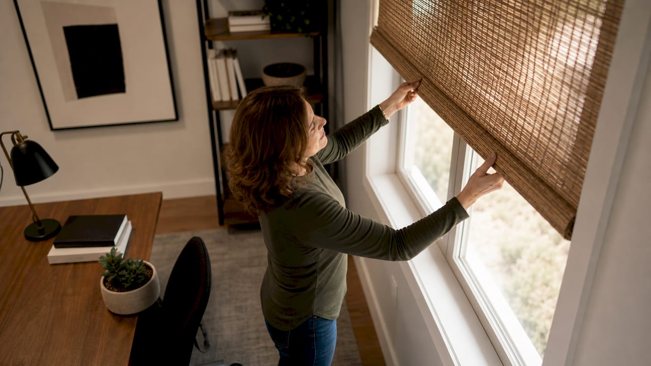 Woman adjusting woven wood window shade in living room